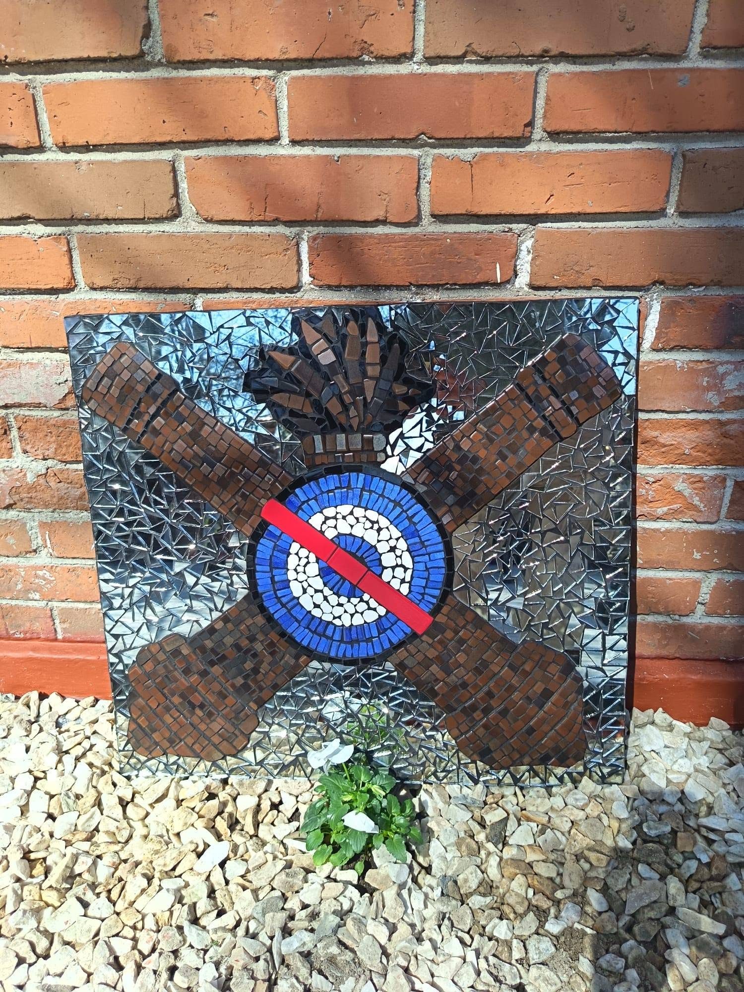 Escudo del Comando de Artillería en mosaico: dos cañones cruzados en cerámica marrón y la escarapela azul, blanca y roja, sobre fondo de espejos.