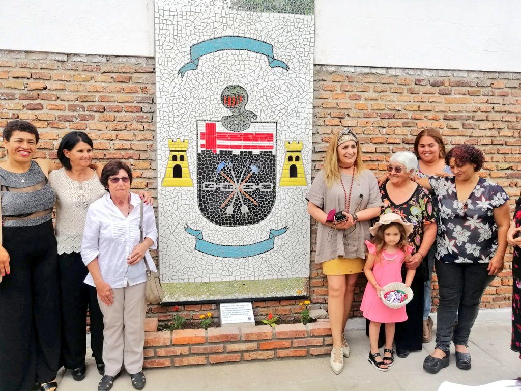 Escudo heráldico del Batallón de Ingenieros de Combate N.º 2 en mosaico sobre una pared de ladrillo, con integrantes del grupo.