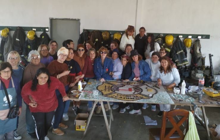 El grupo alrededor de la mesa con el escudo de Bomberos en mosaico, en el cuartel, con los cascos colgados detrás.