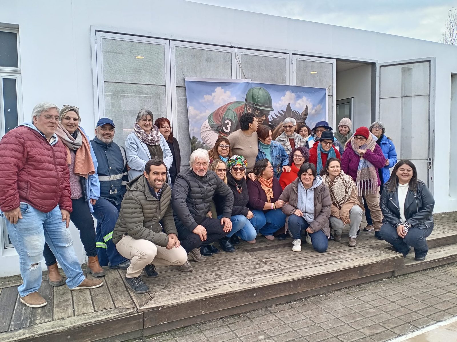 El grupo y trabajadores del hipódromo posan delante del diseño impreso del mural Irineo Leguisamo.