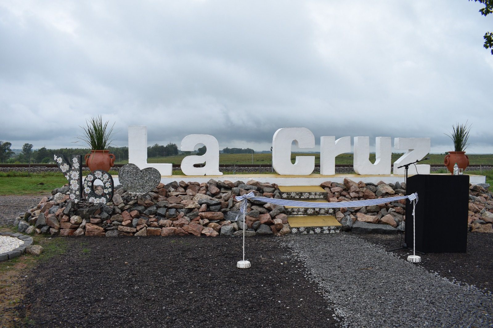 Vista general del monumento de bienvenida a La Cruz, con las letras "Yo" decoradas en mosaico de margaritas y un corazón de espejos junto a las letras corpóreas "La Cruz"; los escalones de acceso también están revestidos en mosaico floral