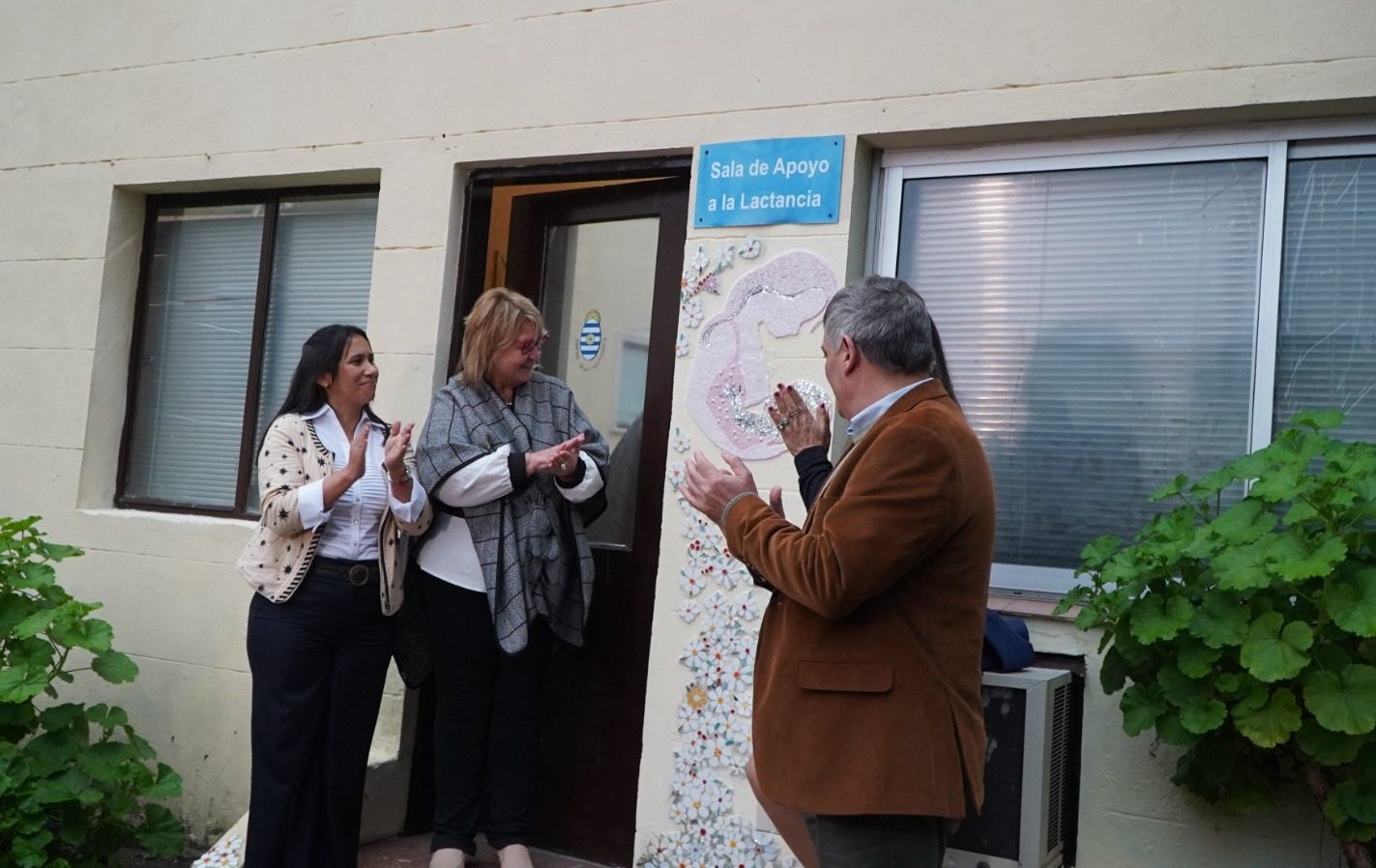 Tres autoridades aplaudiendo en la puerta de la sala, con el mosaico visible a la derecha