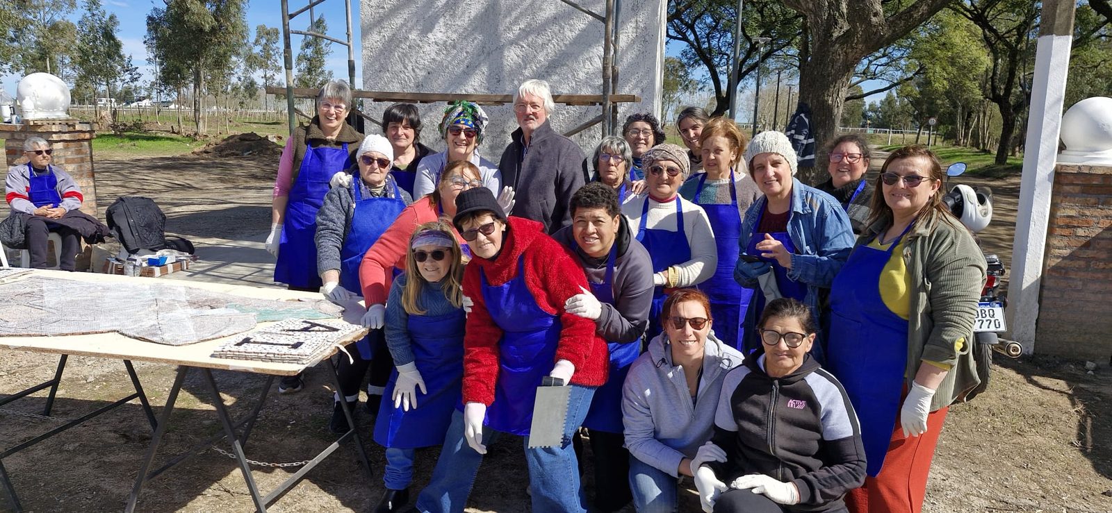 Las integrantes con delantales azules, guantes y espátulas, junto a la mesa donde se arma el mural Irineo Leguisamo.