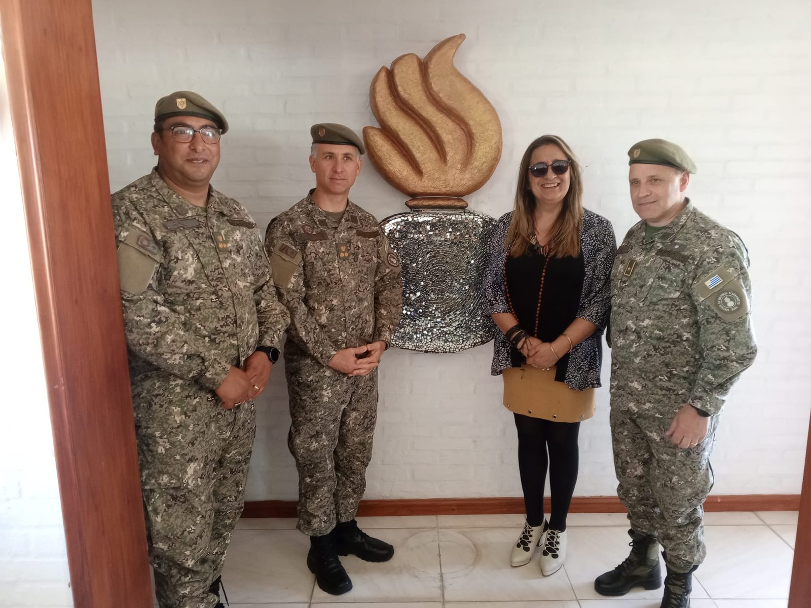 Segundo mural grande: escultura de una llama dorada sobre una base circular de mosaico de espejos, en el hall de la unidad; dos oficiales observan el mosaico