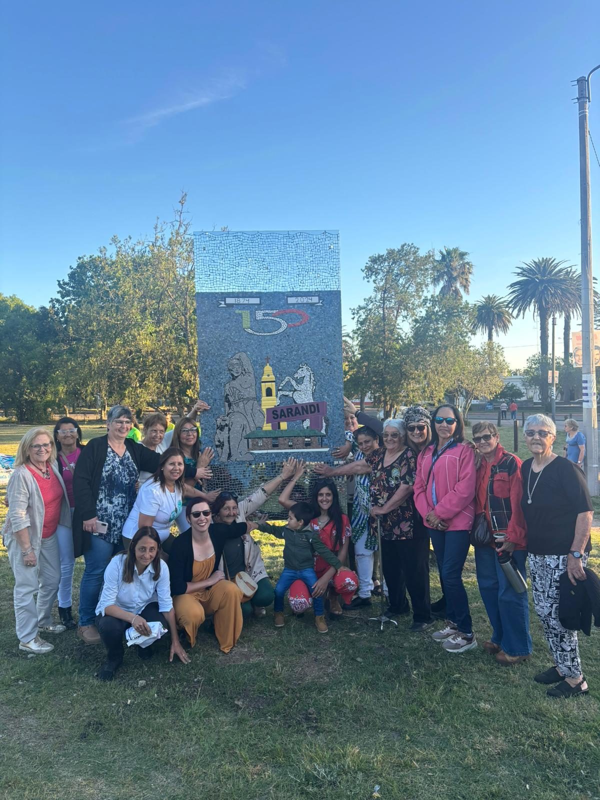 Integrantes de ReciclArte posando frente al panel de mosaico ya descubierto, sobre el pasto de un espacio verde de Sarandí Grande.